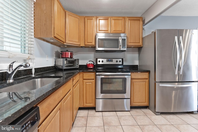 kitchen featuring dark stone countertops, sink, light tile patterned floors, and stainless steel appliances