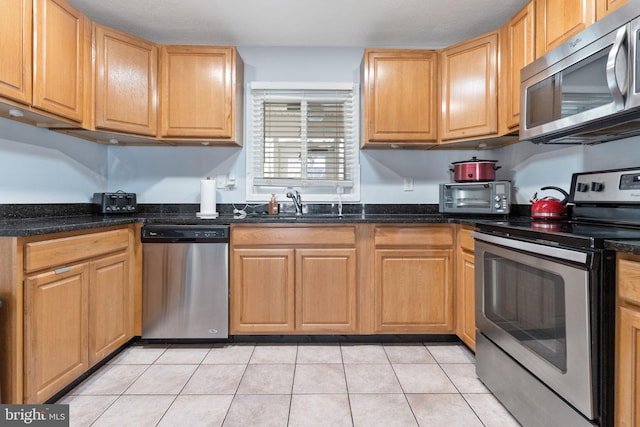 kitchen featuring light tile patterned flooring, appliances with stainless steel finishes, sink, and dark stone countertops