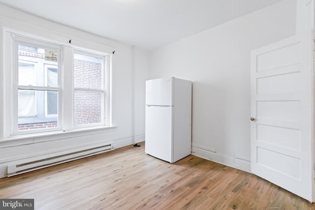 unfurnished bedroom featuring multiple windows, white fridge, light wood-type flooring, and baseboard heating