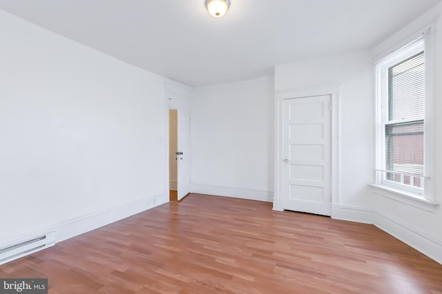 empty room with a healthy amount of sunlight, baseboard heating, and light wood-type flooring