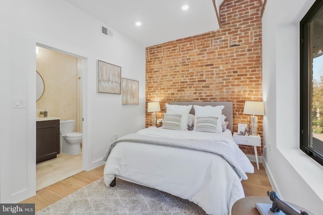 bedroom featuring ensuite bathroom, brick wall, and light hardwood / wood-style floors