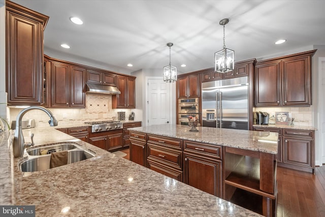 kitchen with sink, appliances with stainless steel finishes, a kitchen island, pendant lighting, and light stone countertops