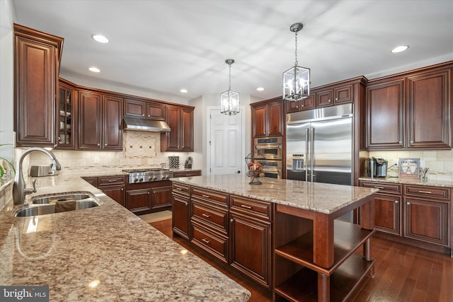 kitchen with sink, decorative light fixtures, appliances with stainless steel finishes, a kitchen island, and light stone countertops