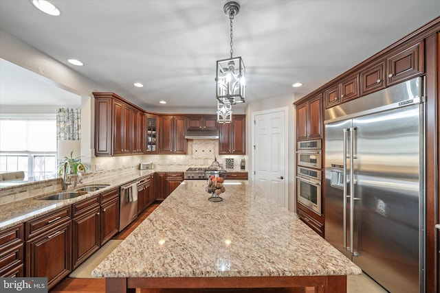 kitchen with sink, hanging light fixtures, a center island, light stone counters, and stainless steel appliances