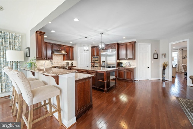 kitchen featuring dark wood-type flooring, light stone counters, decorative light fixtures, kitchen peninsula, and built in fridge