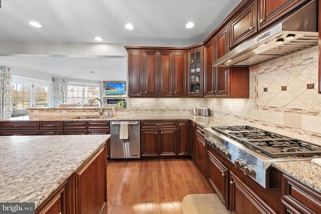 kitchen with sink, appliances with stainless steel finishes, light stone countertops, decorative backsplash, and light wood-type flooring