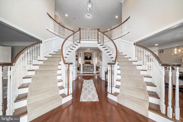 foyer with an inviting chandelier, a towering ceiling, ornamental molding, and dark hardwood / wood-style floors