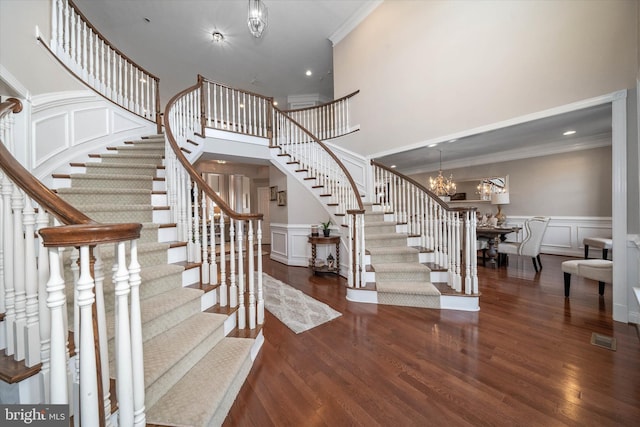 stairs featuring hardwood / wood-style flooring, ornamental molding, a towering ceiling, and an inviting chandelier