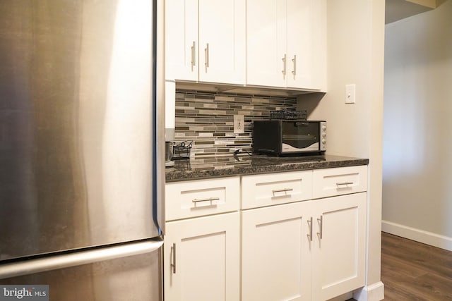 kitchen featuring dark wood-type flooring, white cabinetry, tasteful backsplash, stainless steel fridge, and dark stone counters