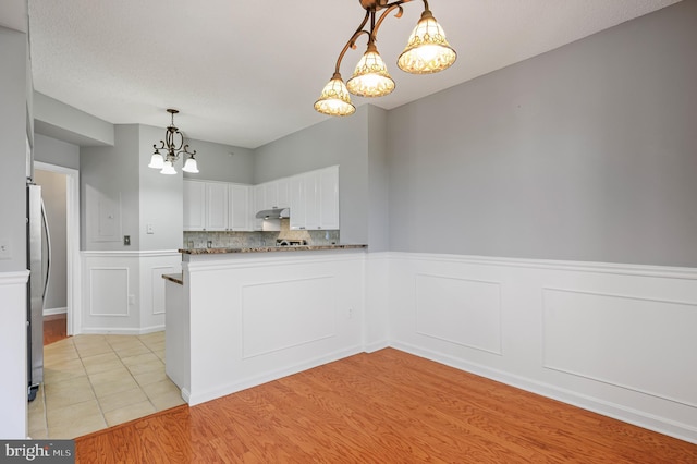 kitchen featuring pendant lighting, stainless steel refrigerator, white cabinets, a notable chandelier, and kitchen peninsula