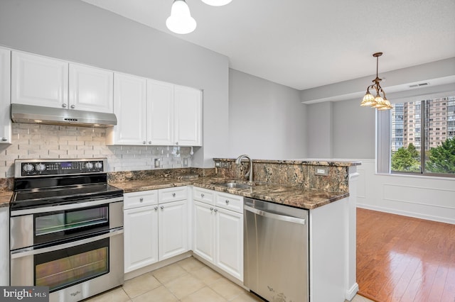 kitchen with appliances with stainless steel finishes, white cabinets, dark stone counters, hanging light fixtures, and kitchen peninsula