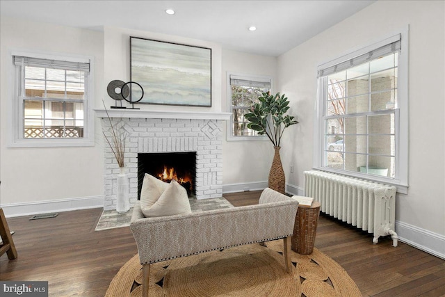 living area featuring a brick fireplace, radiator, and dark hardwood / wood-style flooring