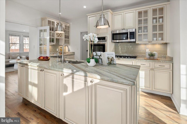 kitchen featuring sink, appliances with stainless steel finishes, a kitchen island with sink, light stone counters, and decorative light fixtures