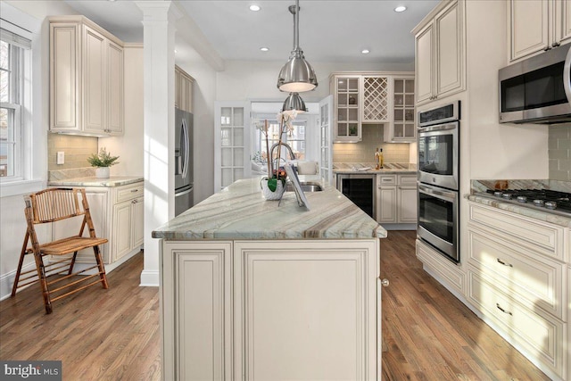 kitchen with a kitchen island with sink, hanging light fixtures, wine cooler, and appliances with stainless steel finishes