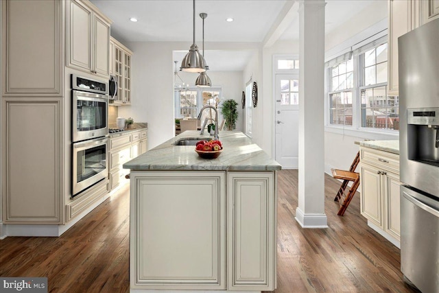 kitchen featuring sink, stainless steel appliances, cream cabinets, an island with sink, and decorative light fixtures