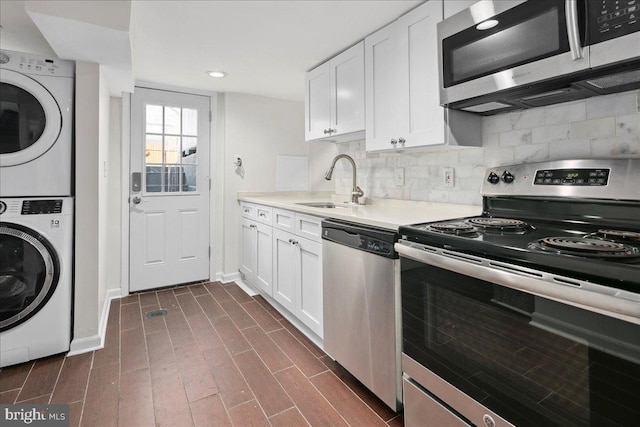 kitchen featuring white cabinetry, stacked washing maching and dryer, appliances with stainless steel finishes, and sink