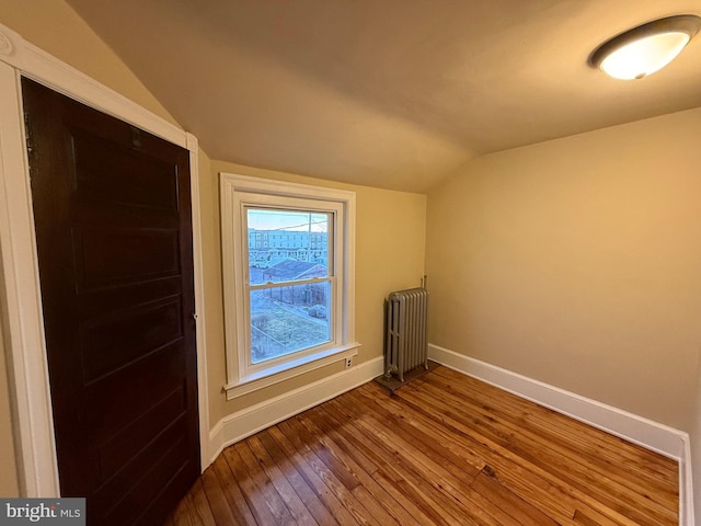 spare room featuring hardwood / wood-style flooring, vaulted ceiling, and radiator