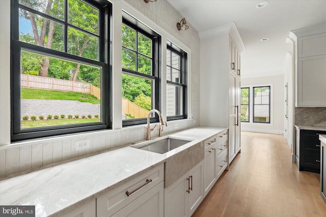 kitchen featuring tasteful backsplash, white cabinetry, a sink, and light stone countertops