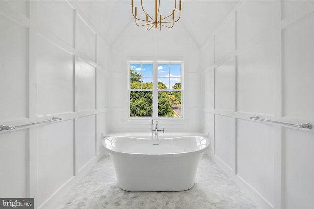 full bath featuring vaulted ceiling, a freestanding tub, a notable chandelier, and a decorative wall