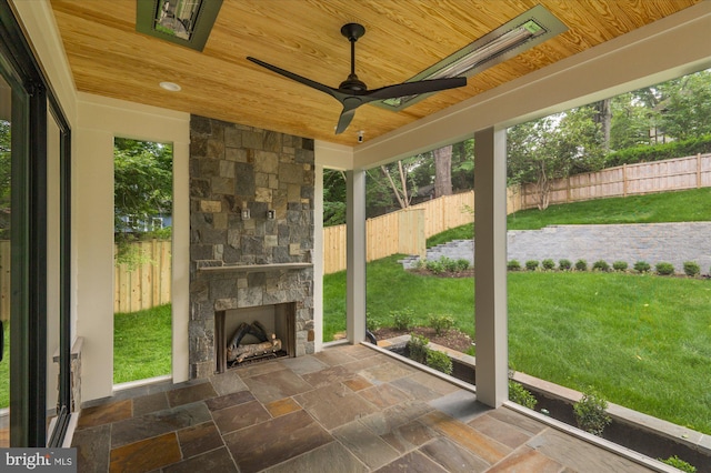 unfurnished sunroom with wood ceiling, a wealth of natural light, and an outdoor stone fireplace