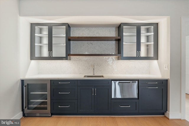 bar featuring wine cooler, backsplash, a sink, and light wood-style flooring