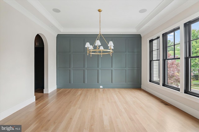 unfurnished dining area with a notable chandelier, a tray ceiling, visible vents, and a decorative wall