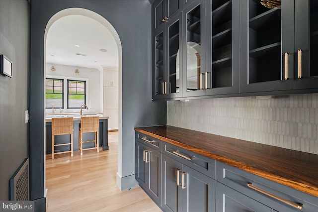 bar featuring arched walkways, backsplash, visible vents, and light wood-style flooring