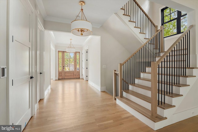 foyer entrance featuring baseboards, ornamental molding, stairway, and light wood-style floors