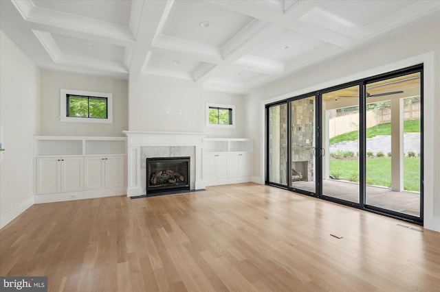 unfurnished living room with beamed ceiling, plenty of natural light, a high end fireplace, and light hardwood / wood-style flooring