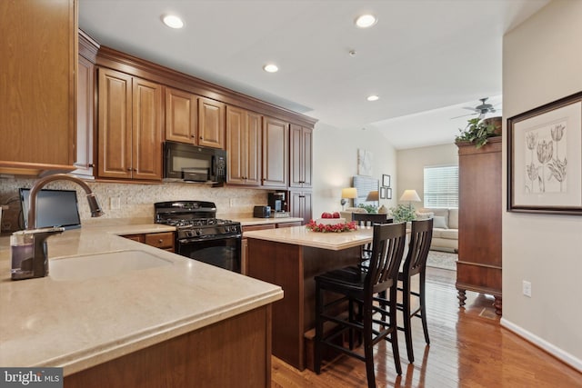 kitchen with sink, a kitchen island, black appliances, a kitchen bar, and decorative backsplash