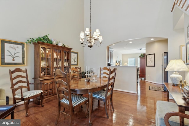 dining area featuring hardwood / wood-style flooring, a towering ceiling, and ceiling fan with notable chandelier