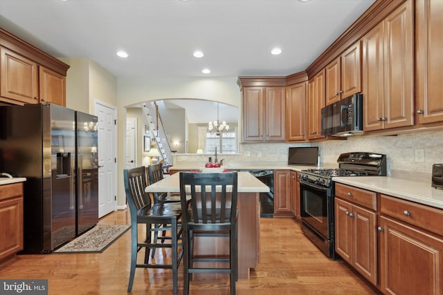 kitchen with an inviting chandelier, light hardwood / wood-style floors, black appliances, and a kitchen breakfast bar