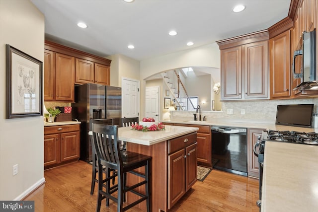 kitchen with sink, a breakfast bar area, black appliances, a kitchen island, and light wood-type flooring