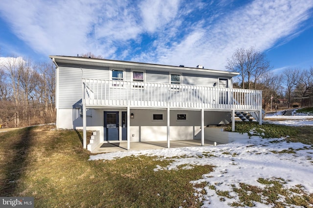 snow covered house with a wooden deck, a yard, and a patio area