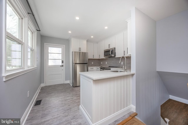 kitchen featuring wood-type flooring, stainless steel appliances, kitchen peninsula, and white cabinets