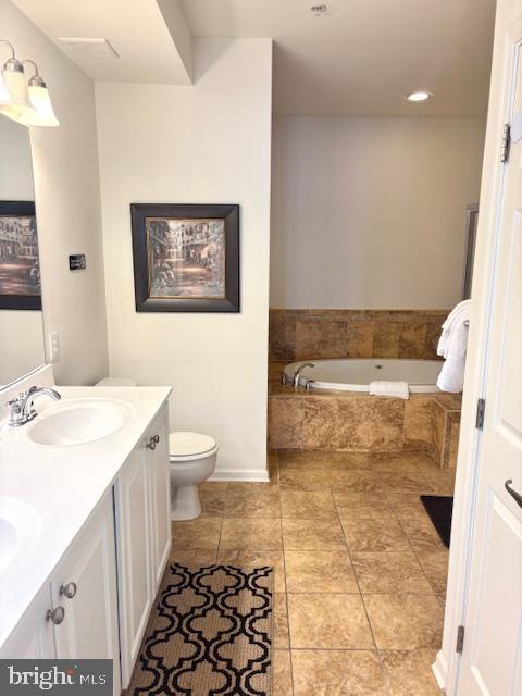 bathroom featuring a relaxing tiled tub, vanity, toilet, and tile patterned flooring