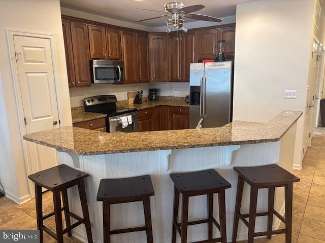 kitchen with light stone counters, a kitchen breakfast bar, ceiling fan, and appliances with stainless steel finishes