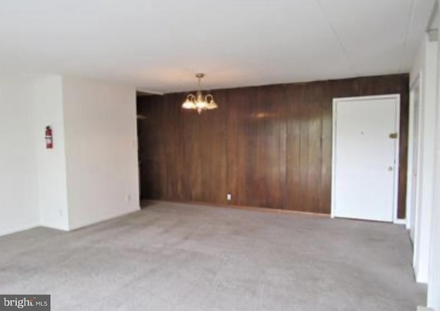 spare room featuring wooden walls, a chandelier, and light carpet