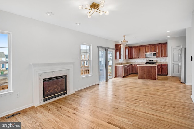 kitchen featuring light hardwood / wood-style flooring, appliances with stainless steel finishes, backsplash, a center island, and a fireplace