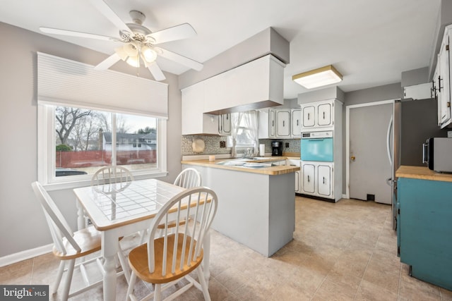 kitchen with white cabinetry, sink, oven, backsplash, and kitchen peninsula