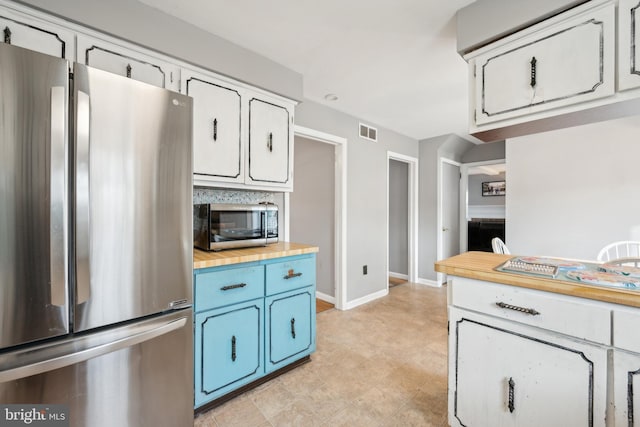 kitchen featuring stainless steel appliances, blue cabinets, wooden counters, and white cabinets