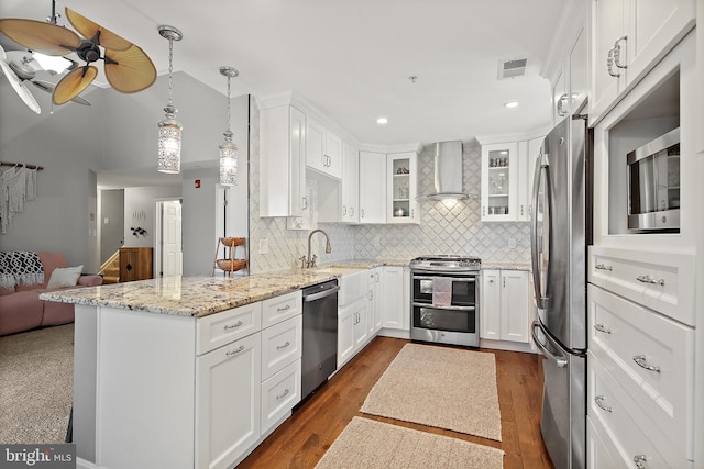 kitchen with stainless steel appliances, white cabinetry, pendant lighting, and wall chimney range hood