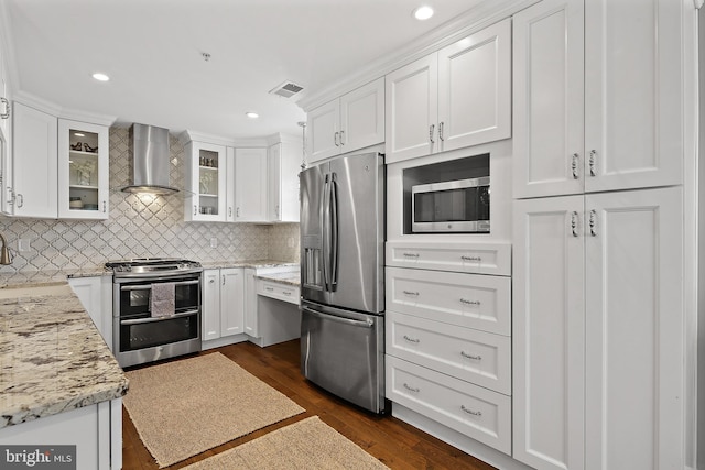 kitchen featuring dark wood-type flooring, white cabinetry, light stone counters, appliances with stainless steel finishes, and wall chimney range hood