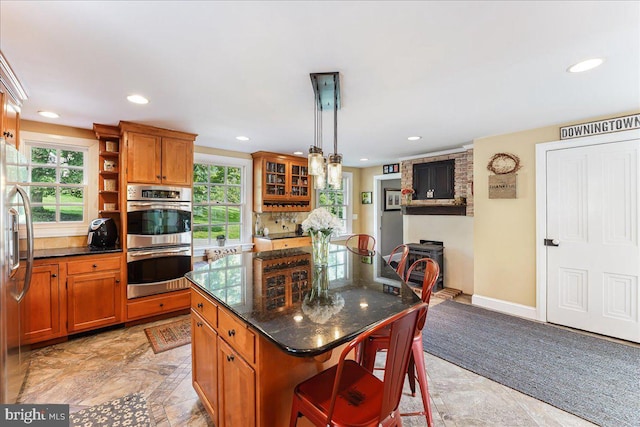 kitchen with a kitchen island, appliances with stainless steel finishes, decorative light fixtures, a kitchen bar, and dark stone counters