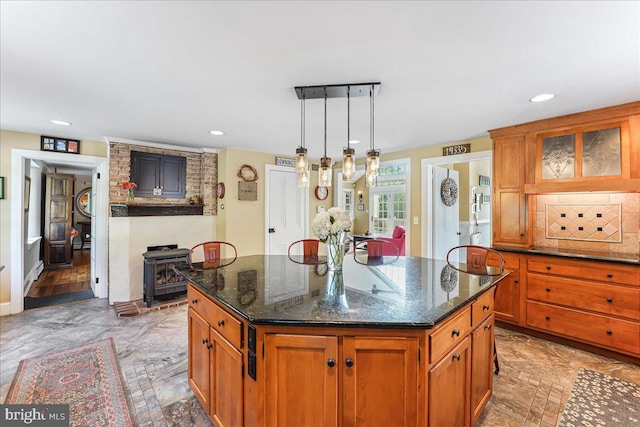 kitchen with a kitchen island with sink, a wood stove, dark stone counters, and decorative light fixtures