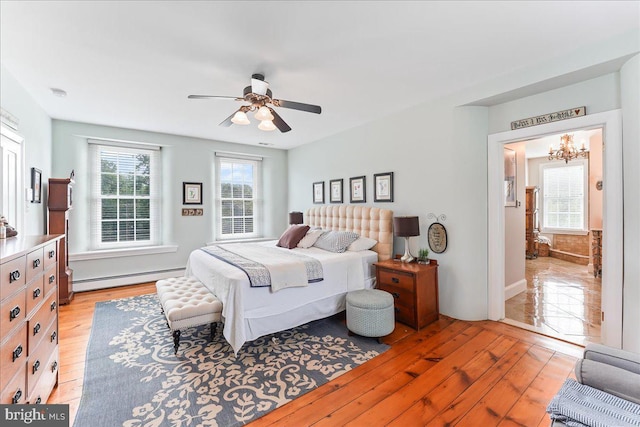 bedroom with light wood-type flooring, ceiling fan with notable chandelier, and baseboard heating