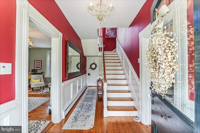 stairs with a notable chandelier, a baseboard radiator, and hardwood / wood-style floors