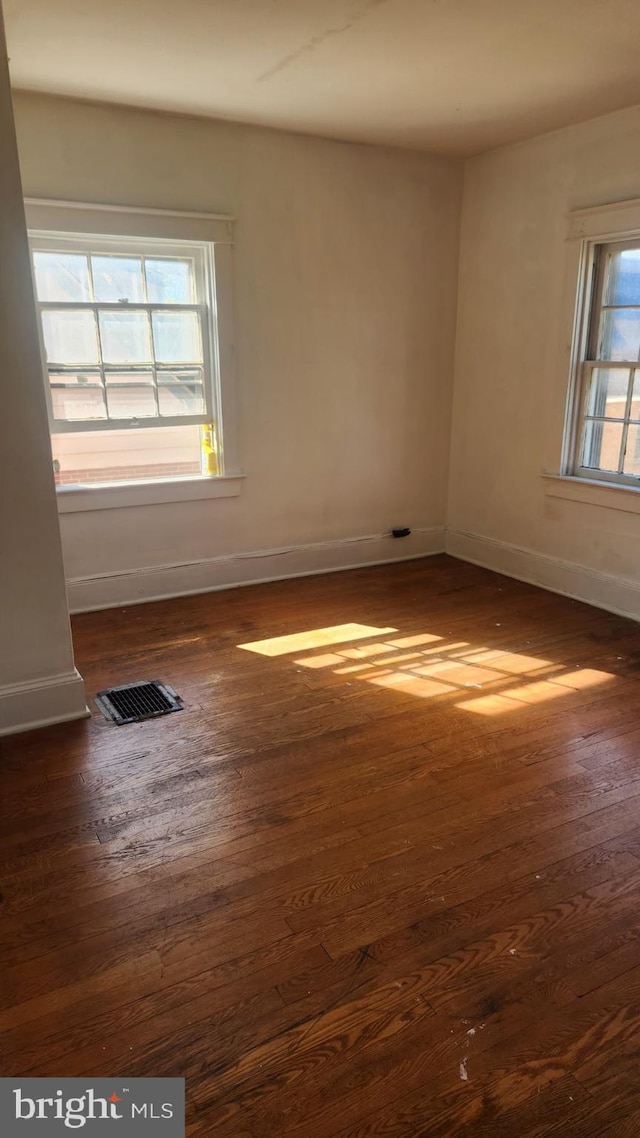 unfurnished room with dark wood-style floors, baseboards, and visible vents