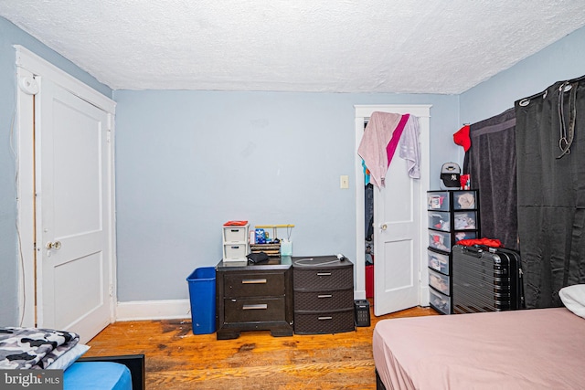 bedroom with a textured ceiling, baseboards, and wood finished floors