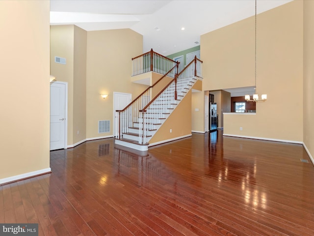 unfurnished living room with an inviting chandelier, wood-type flooring, and high vaulted ceiling